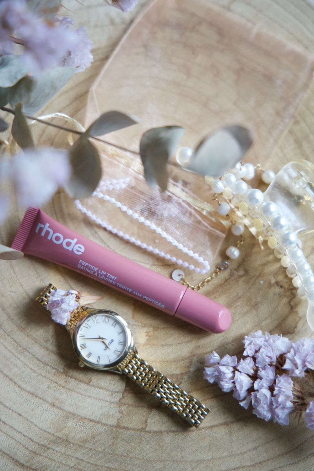 Flat lay with cosmetics, a watch and flowers